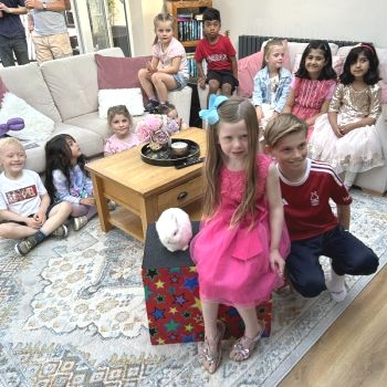The birthday child in West Bridgford beams with joy holding Snowy the rabbit as friends cheer.