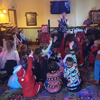 Stuart engaging a room full of laughing children during a live birthday party show in Derbyshire.
